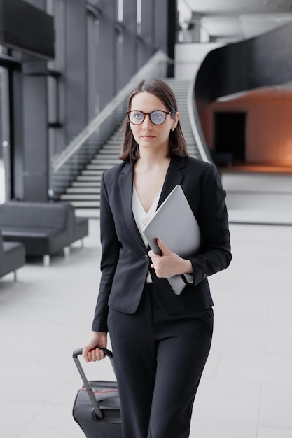 Business tourism business woman in a formal suit with a smartphone in a business center or airport with a suitcase goes on a business trip