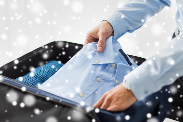 business, trip, luggage and people concept - close up of businessman packing clothes into travel bag over snow effect