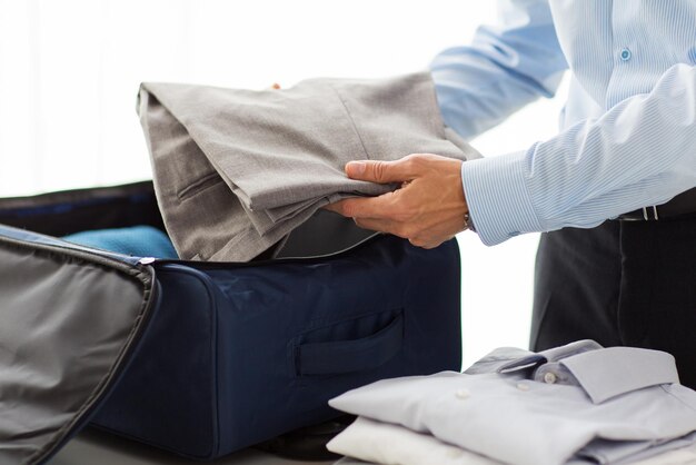 business, trip, luggage and people concept - close up of businessman packing clothes into travel bag