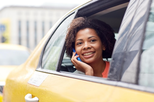 business trip, transportation, travel, gesture and people concept - young smiling african american woman calling on smartphone in taxi at city street