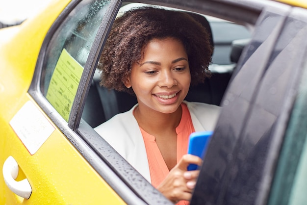 Concetto di viaggio d'affari, trasporti, viaggi, gesti e persone - giovane donna afroamericana sorridente che texing su smartphone in taxi in una strada della città