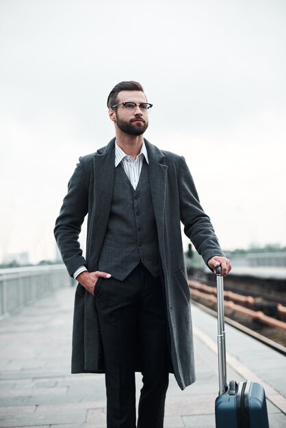 Business trip young businessman walking near railway with luggage confident