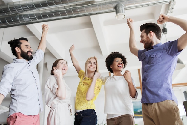 Фото Бизнес, триумф, жест, люди и концепция совместной работы - счастливая творческая команда поднимает руки вверх и празднует победу в офисе