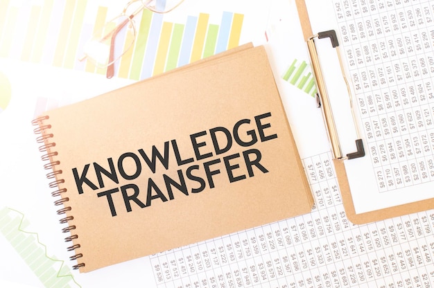 재무 문서가 있는 책상 위에 KNOWLEDGE TRANSFER 메모장이 있는 공예 색상 메모장에 대한 비즈니스 업 그래프