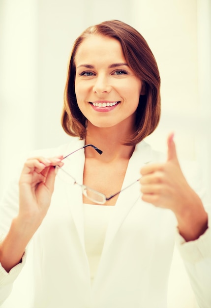 business and vision correction concept - businesswoman with eyeglasses showing thumbs up in office