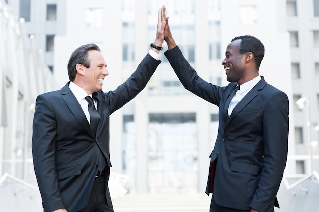 Business winners. Two cheerful business men clapping each other hands and smiling while standing outdoors