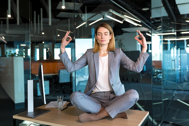 Donna d'affari da sola seduta alla scrivania nel suo ufficio dipendente femminile meditando nella posizione del loto