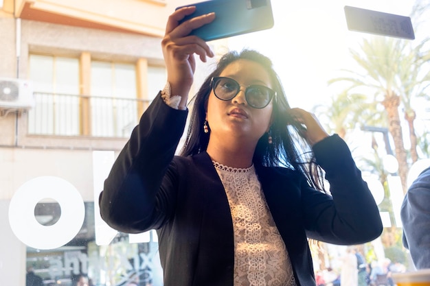 Business woman in a backlit shot looking at her hairstyle on her cell phone