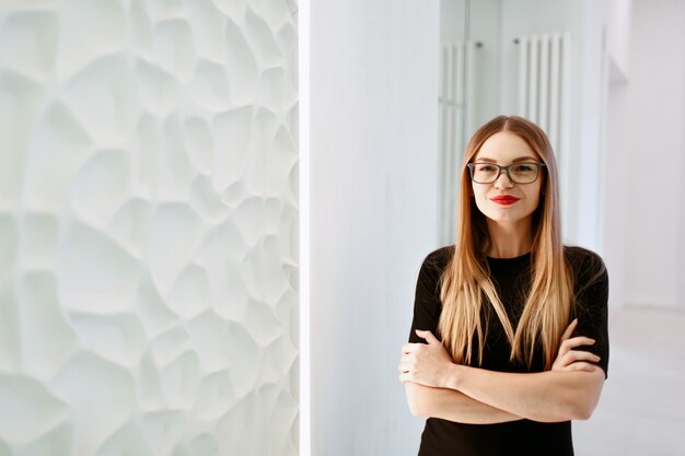 Business woman in black dress looking forward in white office