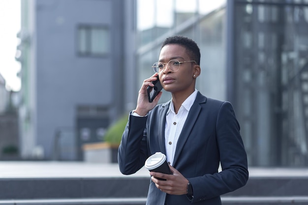 Business woman in business attire talking on the phone African American woman on a break with a cup of hot drink walks in the business district near the office