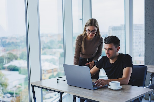 Business woman and businessman are looking for something in the laptop The concept of business cooperation and teamwork Young smiling millennials at the table in the office Modern successful people