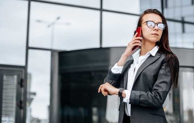 A business woman checks the time and talking on the phone in the city during a working day waiting for a meeting. Discipline and timing. An employee goes towards a corporate meeting.