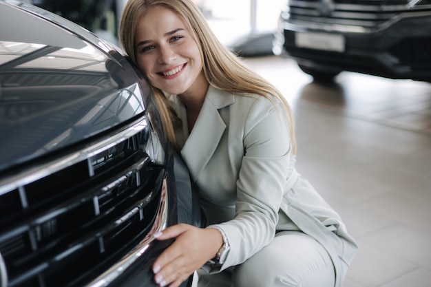 Business woman chossing a new car in a car showroom happy female hug new car and very glad