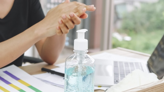 ビジネスの女性は、彼女の机で作業しながら消毒剤アルコールゲルで手を洗浄します。