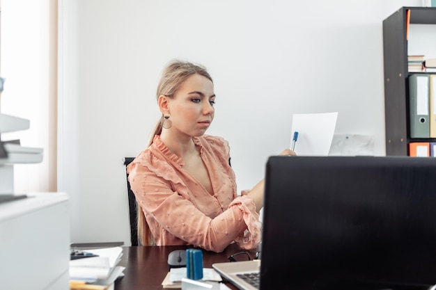 비즈니스 여성은 사무실의 테이블에 앉아 노트북을 들여다보며 화상 통화로 의사 소통합니다. 온라인 회의 화상 통화