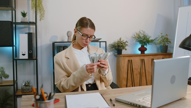 Фото Бизнес-женщина, считающая деньги, наличные доходы, доходы, рассчитывающая финансовые счета, использующая ноутбук в офисе