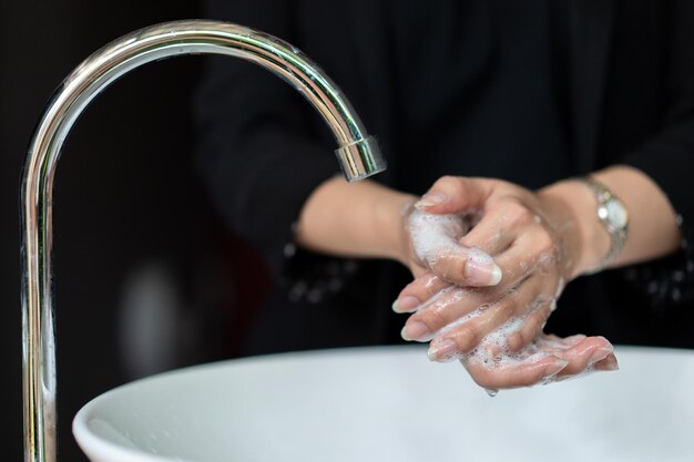 Business woman in dark black suit is washing her hand in sink