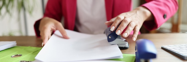 Business woman doing paperwork in office female manager uses document puncher while sitting at