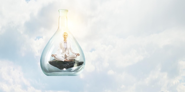 Business woman doing yoga in lotus pose inside glass bottle