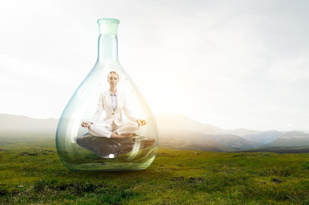 Business woman doing yoga in lotus pose inside glass bottle