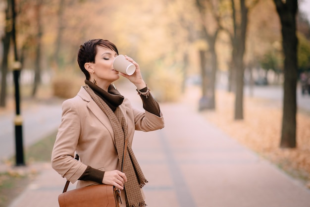 Business woman drinking coffee in autumn street