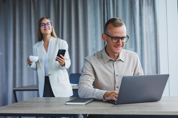 A business woman in front of a male colleague who works at a laptop Business cooperation and teamwork European office workers at the table in the office Modern successful people