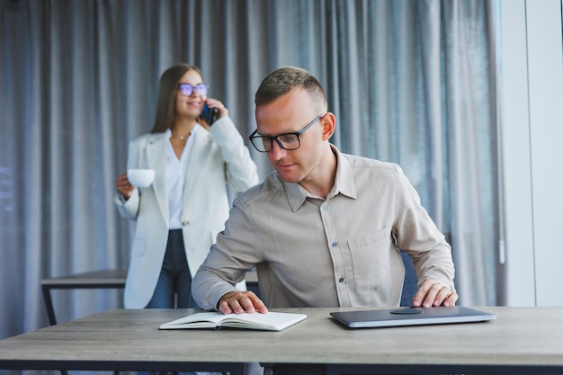 A business woman in front of a male colleague who works at a laptop Business cooperation and teamwork European office workers at the table in the office Modern successful people