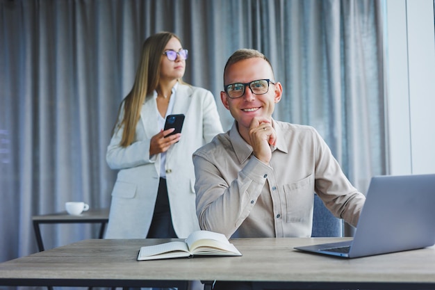 A business woman in front of a male colleague who works at a laptop Business cooperation and teamwork European office workers at the table in the office Modern successful people