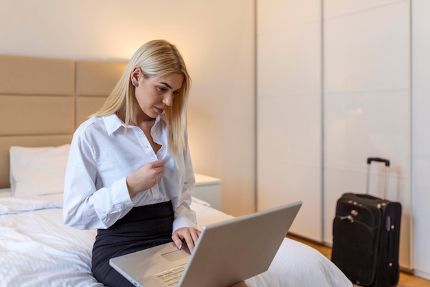 Business woman getting comfortable after work, unbuttoning her shirt and looking at laptop. Businesswoman in hotel room on business trip