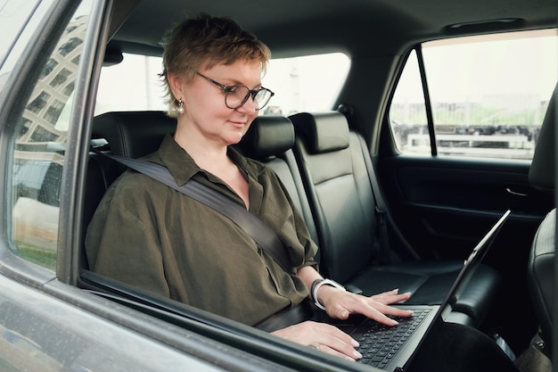 Business woman in glasses is talking on the phone while sitting in the back seat of a car