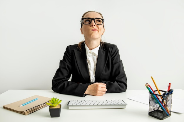 La donna d'affari con gli occhiali guarda pensierosa mentre è seduta sul posto di lavoro