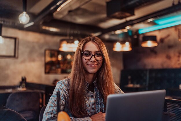 Business woman in glasses sitting in a modern cafe and working on her laptop while drinking a cocktail Selective focus