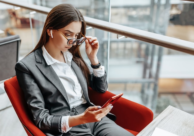 Business woman in glasses at the workplace uses the phone and sits at the table. Manager in the office.