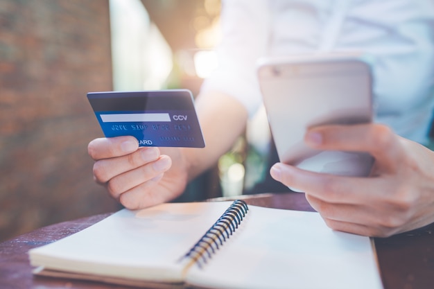 Foto la mano della donna di affari tiene una carta di credito blu e usa i telefoni cellulari.