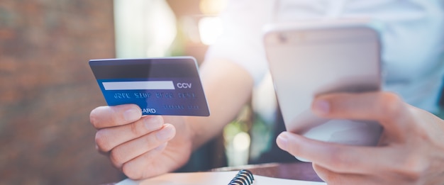 Business woman hand holds a blue credit card and use mobile phones.