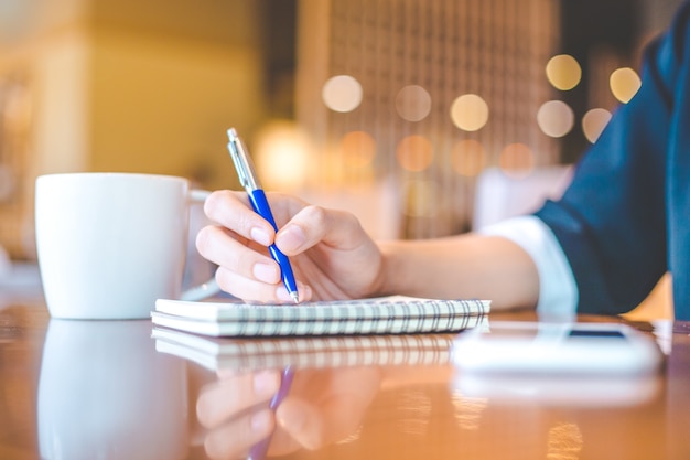 La mano della donna di affari è su un blocco note con una penna su uno scrittorio di legno nell'ufficio.