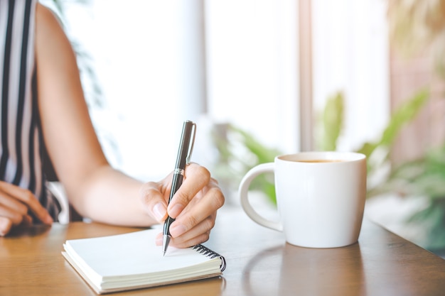 La mano della donna di affari sta scrivendo sul blocco note con una penna nell'ufficio.