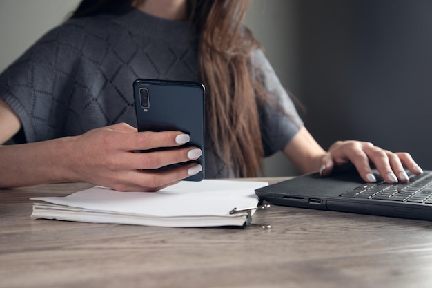 La mano della donna d'affari utilizza un telefono cellulare e lavora in un computer portatile