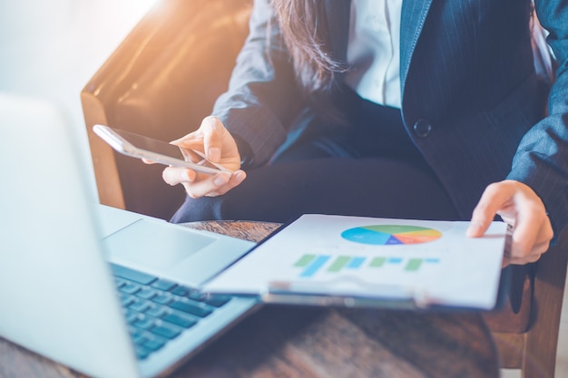 Business woman hand uses a phone to work on charts and graphs that show results.