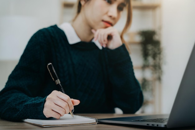 Business woman hand working at a tablet computer and writing on a notepad with a pen in the office