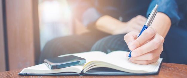 Business woman hand writing on a notepad with a pen.Web banner.