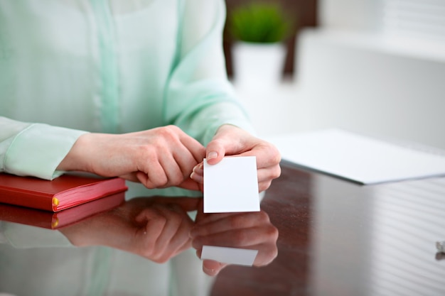 Business woman hands in a green blouse sitting at a desk in an office and holds out business card.