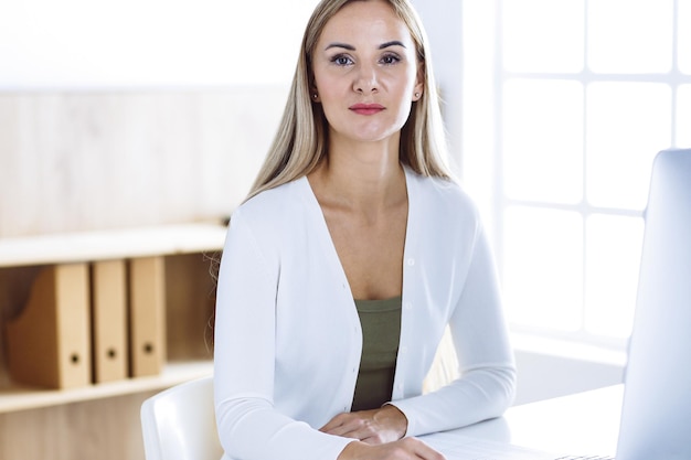 Photo business woman headshot while working with computer at the desk in modern office. designer or female lawyer looks beautiful in white casual clothes. business people concept.