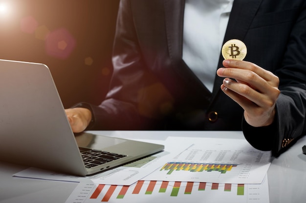 Business woman hold Bitcoin cryptocurrency actual coin in hand to present decentralized finance mockup copy space over black background with computer laptop chart on table