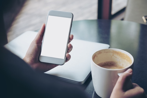 Business woman holding mobile phone with blank white screen with latop