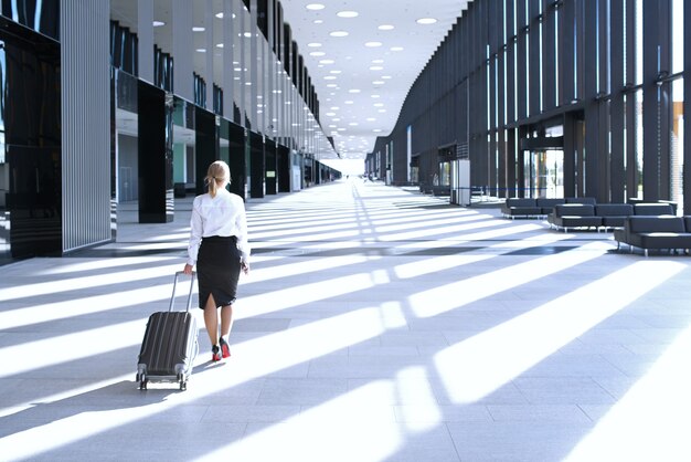 写真 空港ターミナルで車輪付きバッグを持って歩くフォーマルな服を着たビジネスウーマン