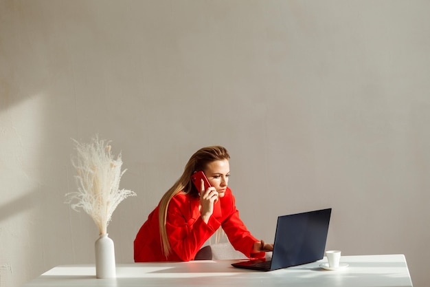 사진 비즈니스 여성이 사무실에서 노트북 흰색 벽 배경을 바라보며 전화 통화를 하고 있습니다.