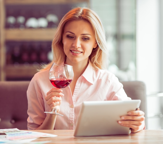 La donna di affari sta usando una compressa e sta bevendo il vino.