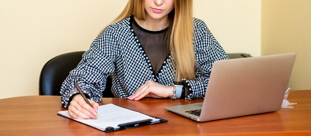 Business woman is writing on a document with laptop at home office.