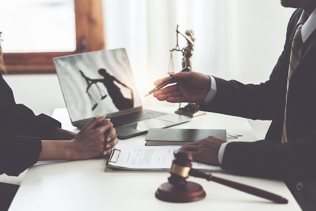 ビジネスの女性と弁護士がオフィスの木製の机の上に真鍮のスケールで契約書を議論する法律法律サービスのアドバイス正義の概念